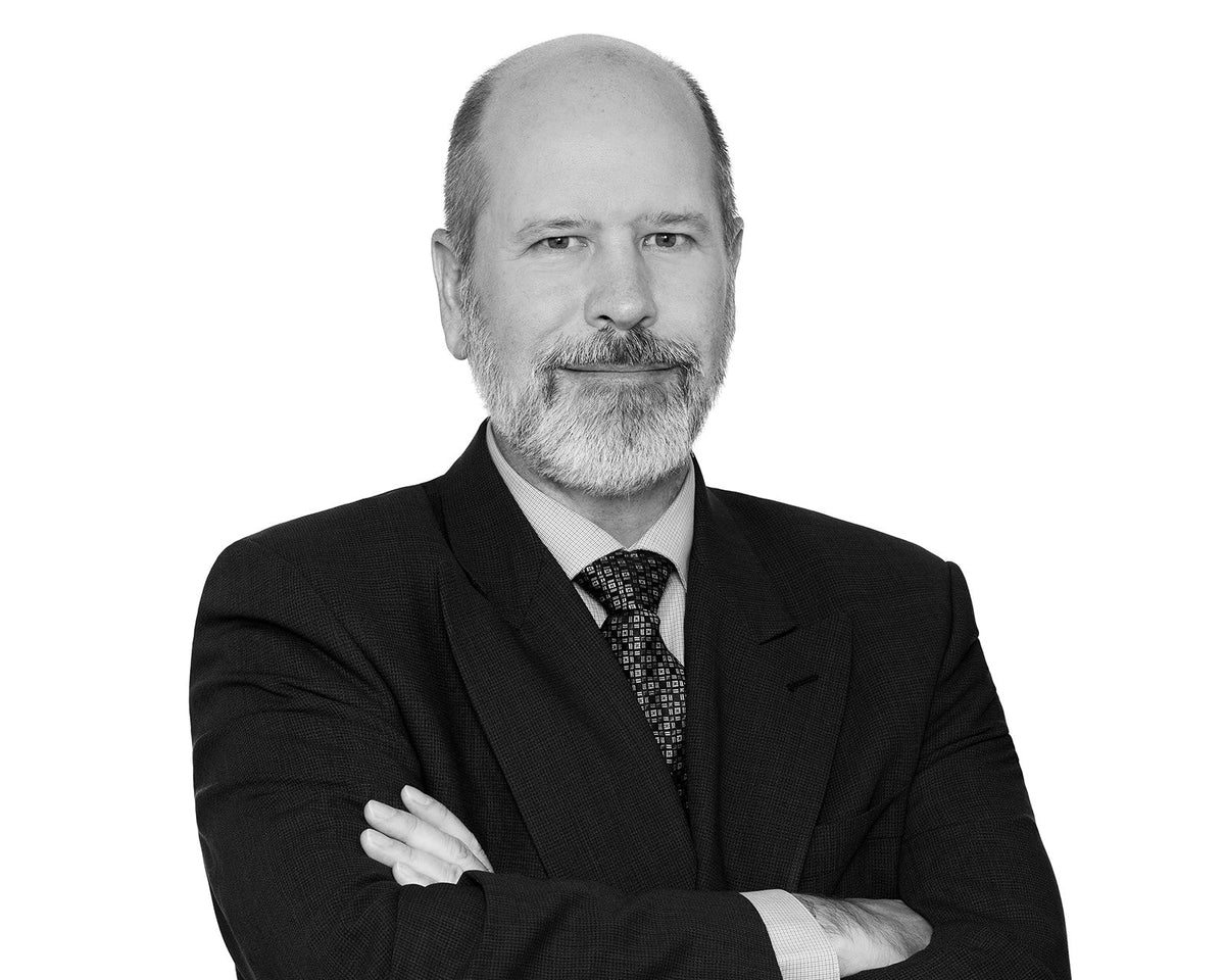 Black and white corporate headshot of a bearded man in a dark suit and patterned tie, arms crossed