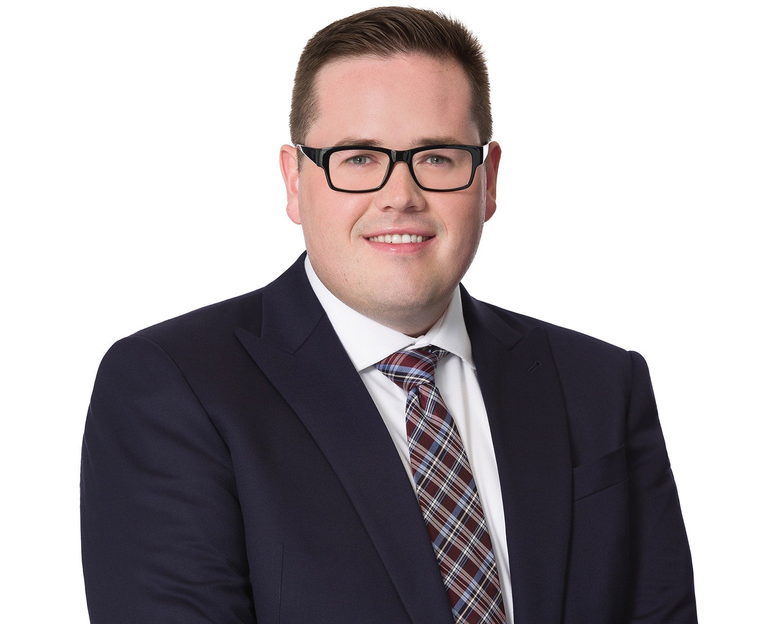 Corporate headshot of a man in a navy suit and glasses on white, naturally retouched and still recognizable