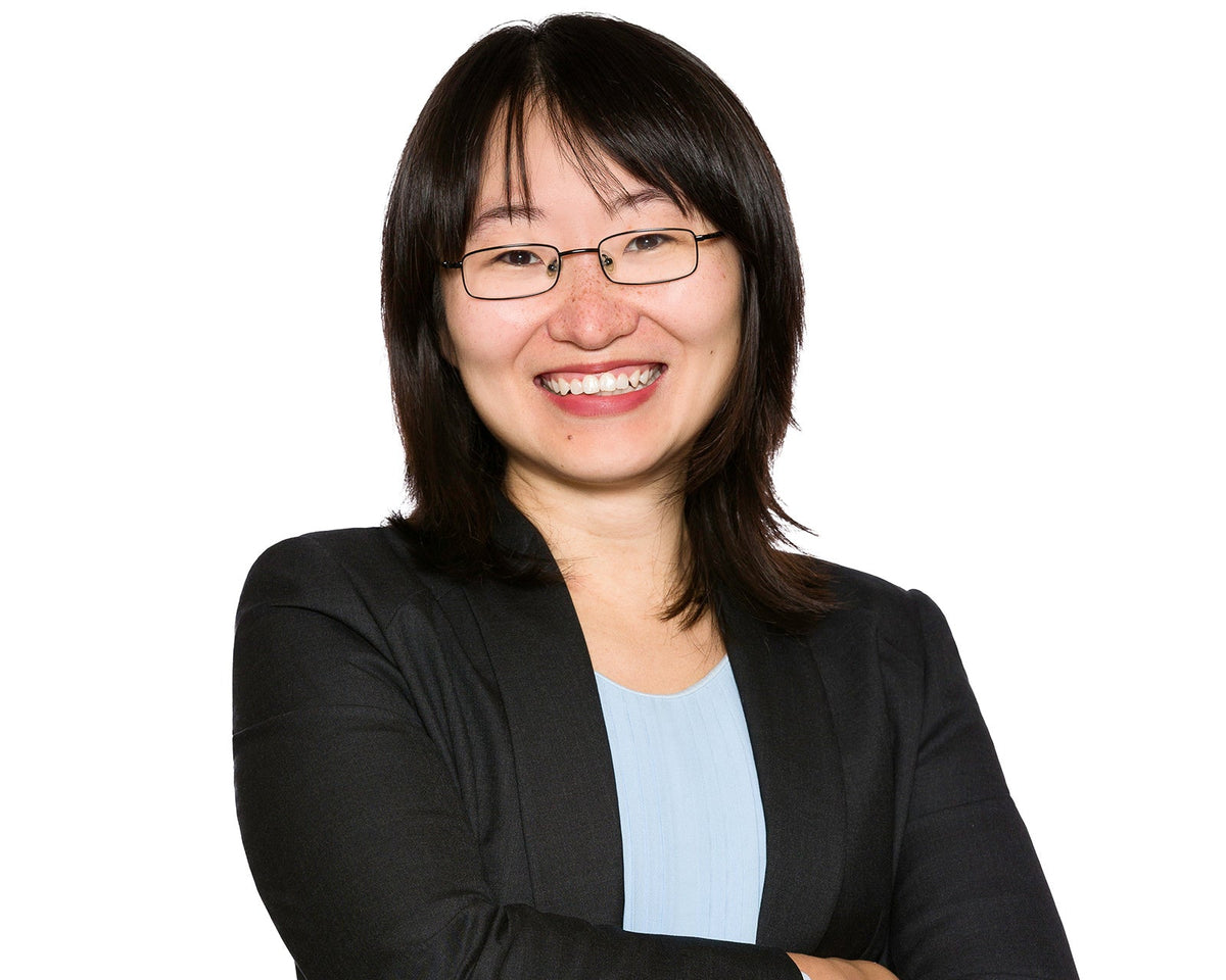 Corporate headshot of a woman in a black jacket and light blue top on a white background