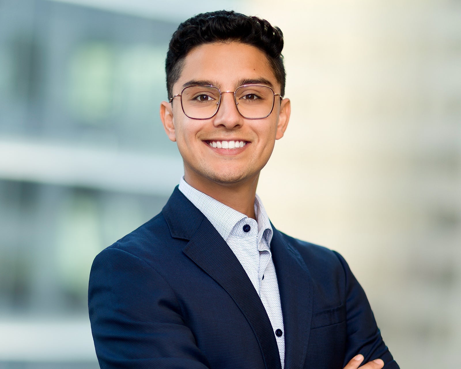 Startup employee in a navy blazer and glasses, arms crossed and smiling, against a blurred downtown Toronto office tower background
