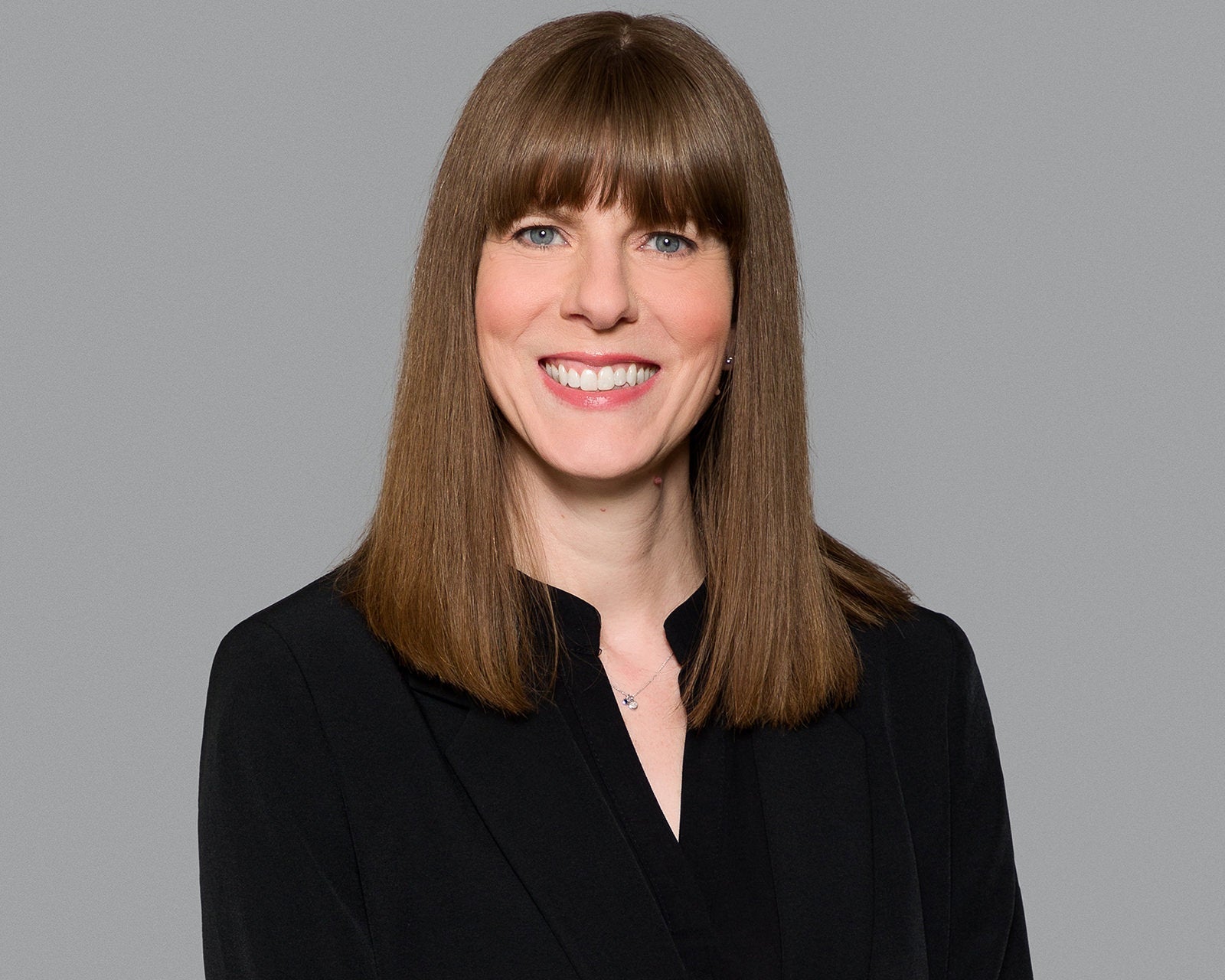 Corporate headshot of a woman in a black blouse on a grey background, with sharp eyes, soft directional light and a natural smile, by BusinessPortraits.ca
